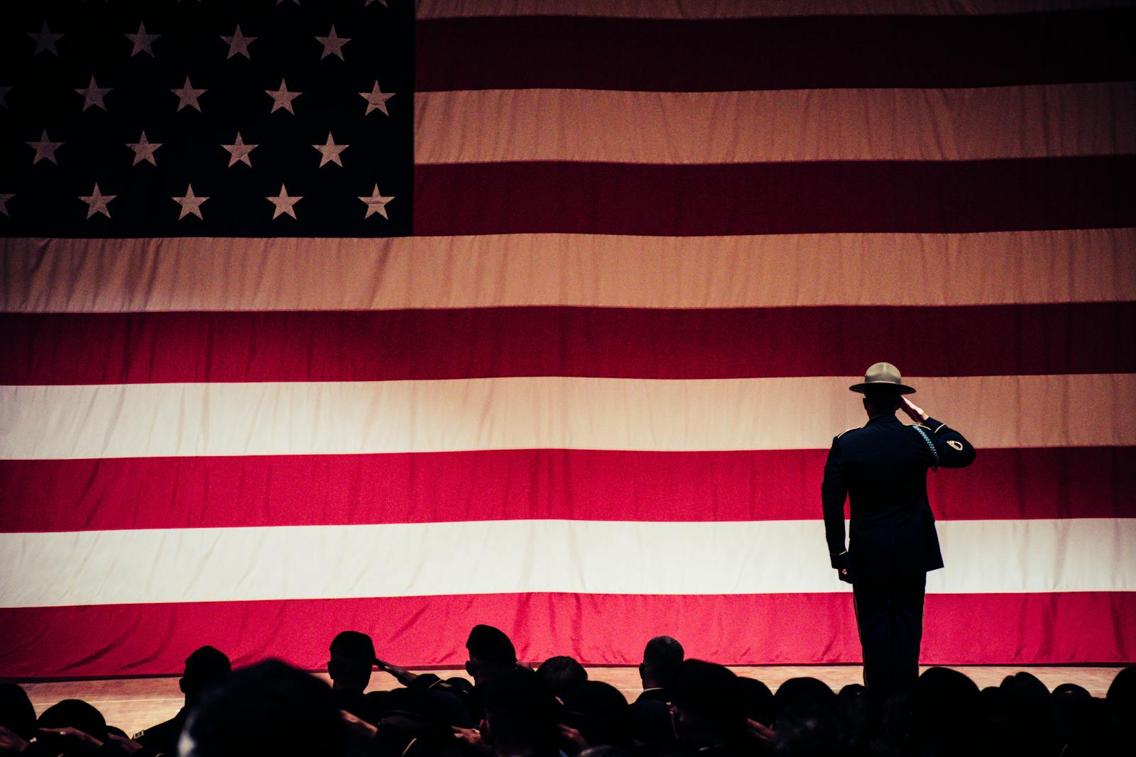 A solemn moment as a soldier salutes the American flag during a ceremony inside an auditorium.